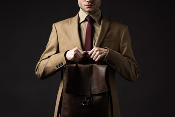 cropped view of elegant man in beige suit holding brown leather backpack isolated on black