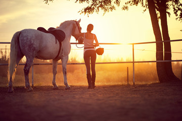 Woman and her horse watching the sunset. Fun on countryside, golden hour. Freedom nature concept.