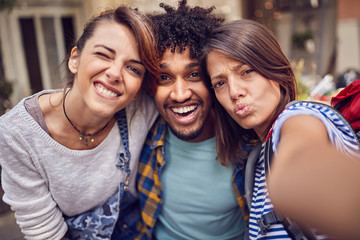 group of young friends looking to phone and taking sefie outdoor.