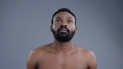 Portrait of topless sexy african american man using a virtual screen swiping pages in air. Young black guy with beard and fit body isolated on grey background.