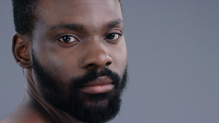 Close-up profile of handsome confident african american man with a beard looking forward isolated on grey background.