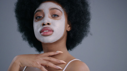 Portrait of elegant african girl model with white mask taking care of skin and beauty indoors. Wonderful black young woman looking at camera isolated on grey background.