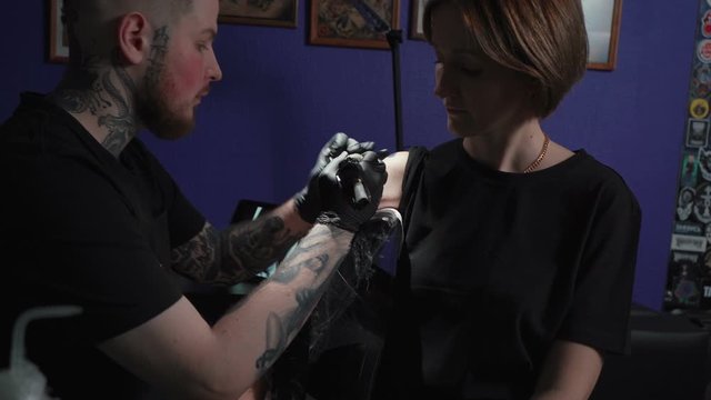 Shooting of man doing black tattoo for woman in studio