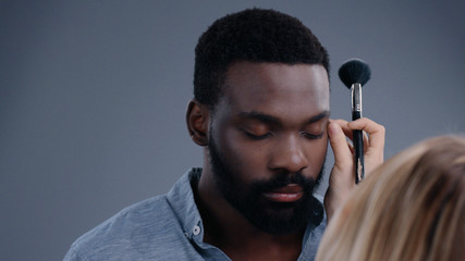 View of professional make-up artist applying concealer on handsome man face with a brush....