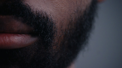 Cropped portrait of handsome afro-american young man model. Close-up on the mouth and chin of an attractive black bearded man over a grey background.