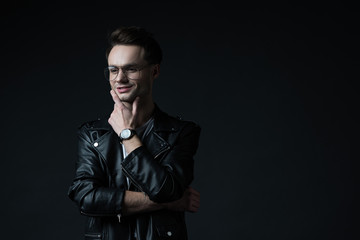 Fototapeta premium smiling dreamy stylish brutal man in biker jacket isolated on black