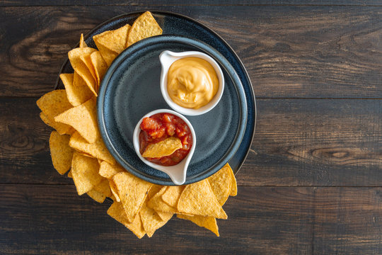 Nachos corn chips on blue plate with salsa and cheese dip on a wooden rustic table, top view, flat lay, copy space. Beer crispy snack, traditional Mexican food.