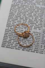 Wedding rings lie on the page of an open Bible. In the center of the ring the phrase is visible: God is Love.