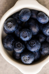 Blueberry in small white plate on a grey background. Macro photo