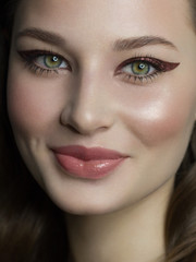 Beautiful brunet model woman face with green eyes and perfect make-up make smile on camera. Portrait of beauty with natural lips and eyes liner, thick eyesbrow . Female face with clear skin close-up.