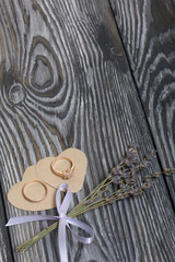 Wedding rings lie on hearts cut out of paper. Near a bunch of lavender. On brushed pine boards painted in black and white.