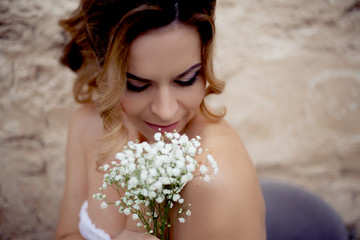 Beautiful woman posing with close eyes  perfect makeup, nude lips and wedding hairstyle. Face portrait of pretty middle aged model holding flowers