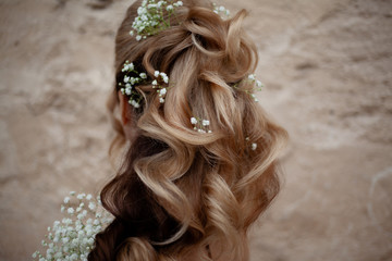 Naklejka premium Blond woman with beautiful log hair on nude shoukders. The hairstyle of bride qith flowers , back view of salon hair do against wall. Care and beauty of hair