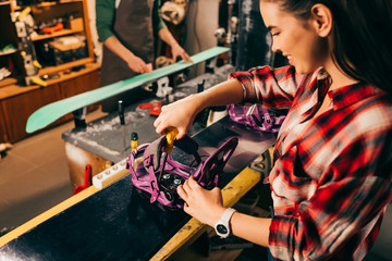 selective focus of smiling worker screwing snowboard binding to snowboard in repair shop