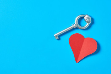 One red paper heart near silver vintage key lies on blue countertop. Concept of closed or opened love or Valentines day. Space for text. Top view. Flat lay