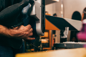 cropped view of worker repairing ski with belt sander in repair shop