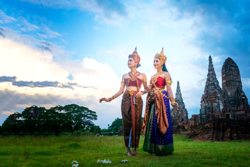 Obraz premium Portrait of an Asian Women in Thai Traditional dancer Clothes are Standing Against Ancient buddha statue. Ayuttaya Historical Park, Thailand Asia.