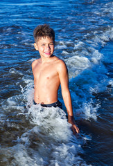 Fototapeta premium Happy smiling boy in the waves of the Baltic Sea on a bright summer day in Jurmala, Latvia