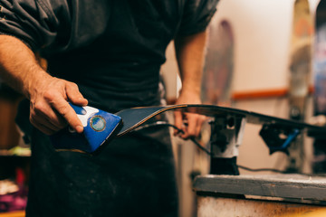 cropped view of worker using wax iron on ski in repair shop