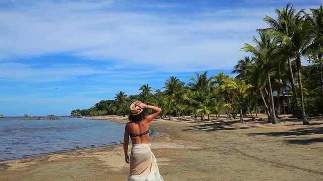 A young woman walking along a beach in the Caribbean Sea on the island of Roatan. Honduras