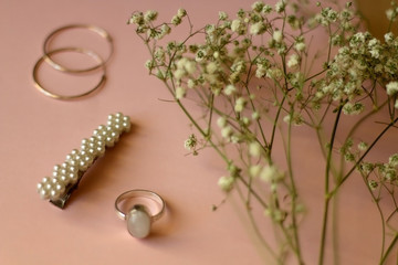 Fashionable accessories on pale pink background. Beret with pearls, silver gemstone ring and hoop earrings, with gypsophila flowers. Selective focus.