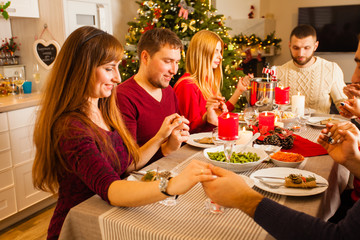 Friends holding hands and praying while having christmas dinner at home