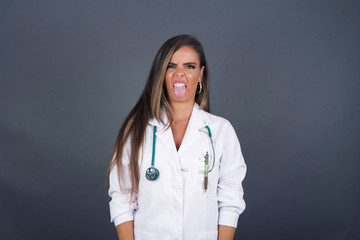 Body language. Disgusted stressed out pretty doctor girl with straight fair hair posing against gray wall, frowning her face, demonstrating aversion to something.