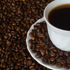 White Cup of black Americano coffee on a background of coffee beans. close-up fragment. A strong, invigorating drink for Breakfast. Copy space