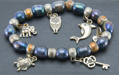 Bead bracelet with hanging metal elements in the form of an elephant, owl, fish, beetle and key. Female decoration on a black background. Bijouterie.