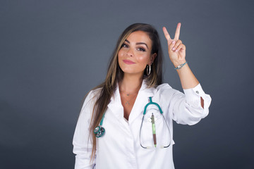 Young doctor woman wearing medical uniform standing against gray wall showing and pointing up with...