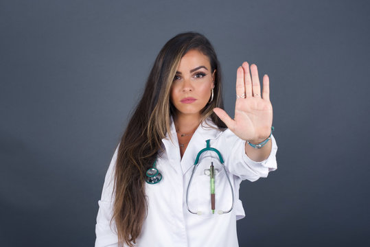 Young beautiful caucasian doctor woman doing stop gesture with palm of the hand. Warning expression with negative and serious gesture on the face isolated over gray background.