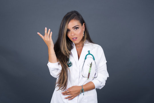 What the hell are you talking about, nonsense. Studio shot of frustrated doctor female gesturing with raised palm, frowning, being displeased and confused with dumb question over gray wall.