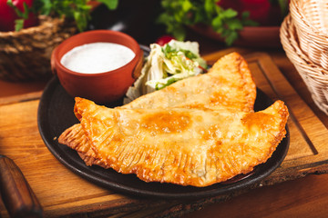 Traditional Crimean Tatar food chebureks with minced meat served with sour cream on black plate.