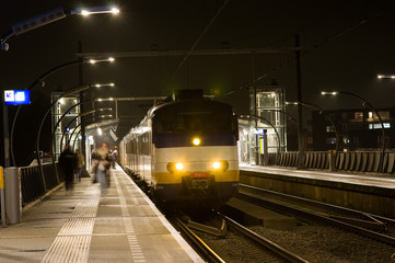 Train is waiting on platform and passengers are getting on and off at night, Netherlands