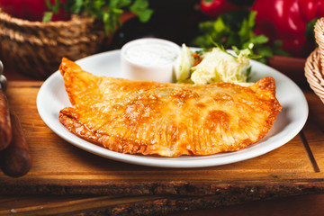 Traditional Crimean Tatar food chebureks with minced meat served with sour cream on white plate.