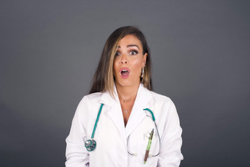 Emotional attractive female with opened mouth expresses great surprisment and frighteness, poses against white concrete background, stares at camera. Unexpected shocking news and human reaction.