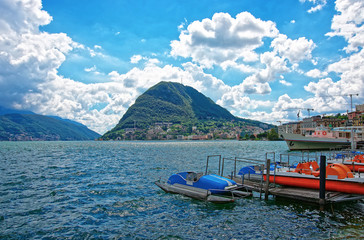 Boats at the landing stage at the promenade of the luxurious resort in Lugano on Lake Lugano and Alps mountains in Ticino canton in Switzerland.