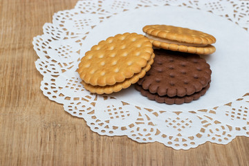 A round shortbread biscuit with cream lies on a paper napkin with beautiful lace edges. Dessert for tea or coffee, children's treat.