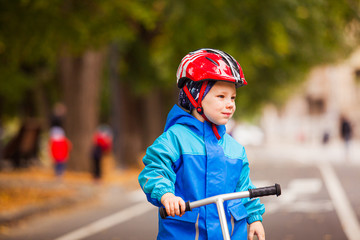 Fototapeta na wymiar Cute preschooler boy in safety helmet riding a scooter.