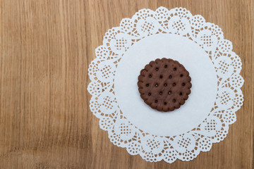 Obraz na płótnie Canvas A round shortbread biscuit with cream lies on a paper napkin with beautiful lace edges. Dessert for tea or coffee, children's treat.