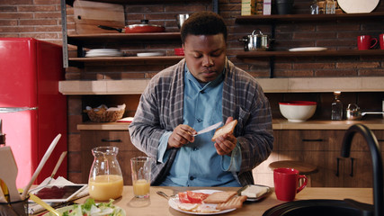 Young afro-american black handsome guy cooking in the kitchen buttering toasts with jam preparing...