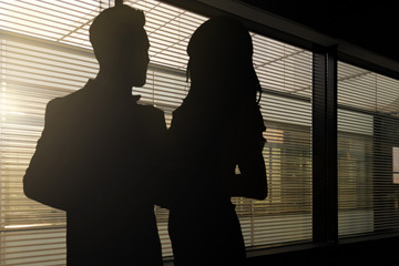 Concept image of romance at work - silhouettes of a woman and a man hugging each other in a dark corporate office