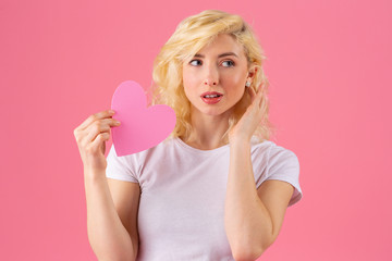 Studio portrait of a young woman pointing at pink heart looking to side