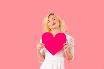 Studio portrait of a young woman holding pink heart with eyes closed, romantic love, dating and Valentine's Day concept