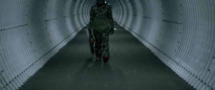 Portrait of a snowboarder in a full face protective helmet walking with a snowboard inside a dark narrow tunnel on a ski resort. 4K UHD RAW graded footage