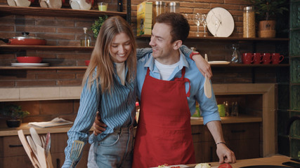 Obraz premium Smiling young couple cooking food in the kitchen laughing fun talk together leisure enjoy dinner preparation at home.