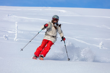 Fototapeta na wymiar Girl On the Ski. a skier in a bright suit and outfit with long pigtails on her head rides outside of the track with swirls of fresh snow. ski freeride, downhill in sunny day. Heliboarding skiing