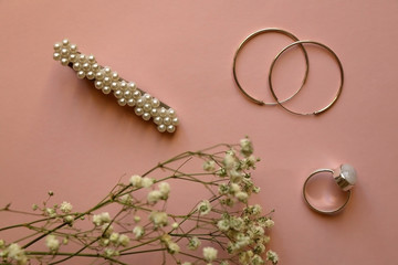 Fashionable accessories on pale pink background. Beret with pearls, silver gemstone ring and hoop earrings, with gypsophila flowers. Top view.