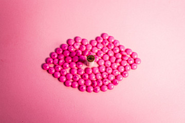 Mouth, made of pink pills and a hand on pink backdrop, text can be added