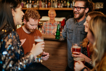 Group of friends drinking beer, chatting and having good time at pub. Night out.